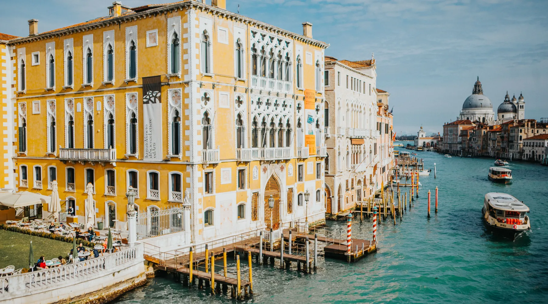 A Grand Canal view in Venice in soft light, with pale palazzi, a domed church in the distance and boats on the water